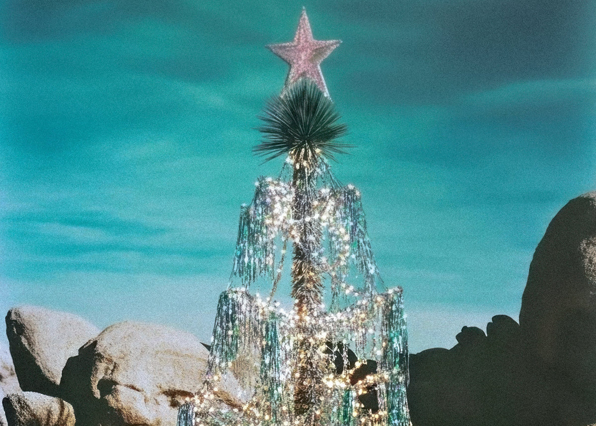 Decorative Christmas tree with lights and a star on top, set against a blue sky and rocky landscape.